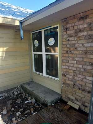 House exterior with a window, brick wall, siding, and a small concrete step beside debris on the ground