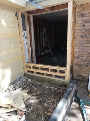 Damaged doorway with exposed framing and debris in front of a brick and siding exterior wall