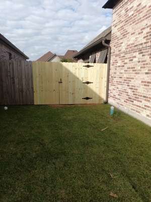 Backyard with a wooden fence, brick wall, and grass lawn under a cloudy sky