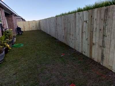 Long narrow backyard with a wooden fence, grassy lawn, and a brick house edge on the left.