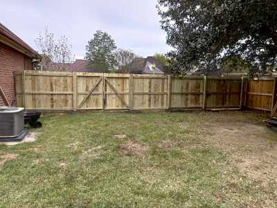 Backyard with patchy grass, wooden privacy fence, and brick house edge on the left