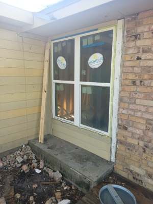 Damaged basement window with broken panes and debris outside a brick wall
