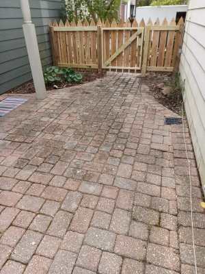 Paver walkway leading to a wooden gate between two houses in a small backyard courtyard