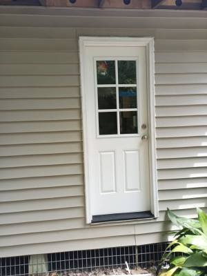 White exterior door with small window on a beige-sided house, above a basement vent.