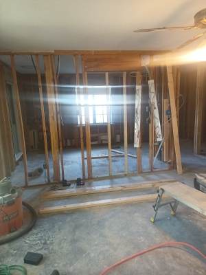 Interior under renovation with exposed wall studs, debris on the floor, and daylight through a window.
