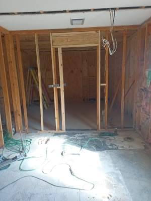 Unfinished room with exposed wooden framing, open doorway, and electrical wires on the floor.