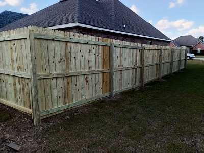 Wooden privacy fence along a backyard beside a house, under a cloudy sky