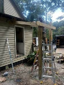 Aluminum ladder and wooden frame under construction beside a beige house and open doorway.