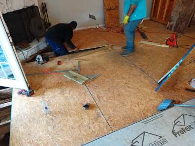 Workers installing floor boards in a room under renovation, with tools and debris on the floor.