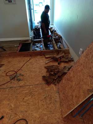 Person working on a floor demolition in a room with exposed subfloor and debris.