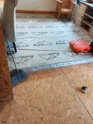 Partially installed flooring with underlayment, tools, and a red tool case in a room under renovation