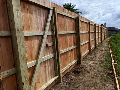 Wooden privacy fence along a muddy yard under construction, stretching into the distance.