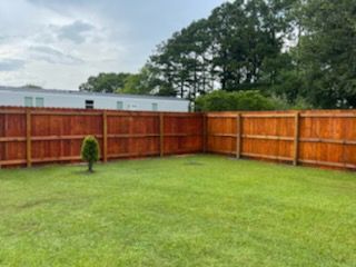 Grassy backyard with a wooden privacy fence and a small shrub near the left side.