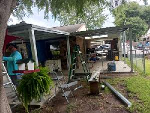 Outdoor patio with potted plants, a ladder, and a person standing near a small covered work area.
