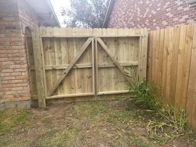 Wooden backyard gate between brick and wood fences over a patchy grass yard