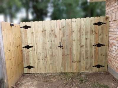 New wooden fence gate with black hinges, centered in a fenced backyard