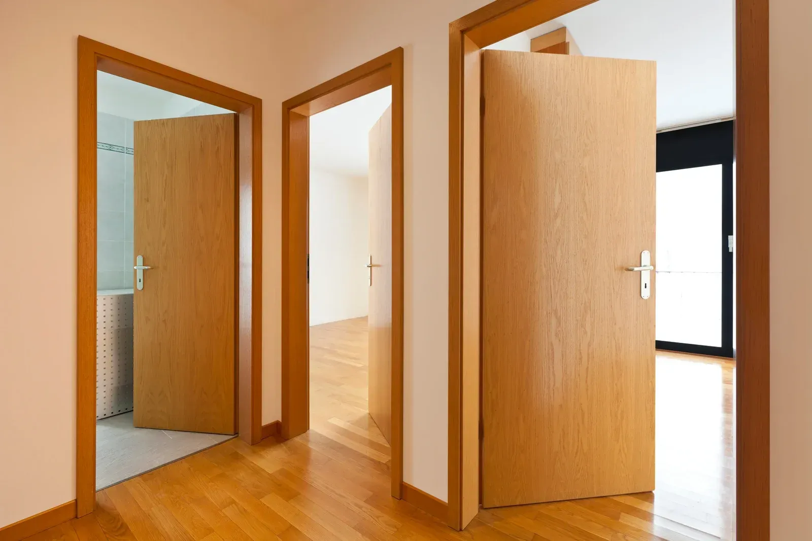 Three wooden doors open into different rooms, in a hallway with wood flooring.
