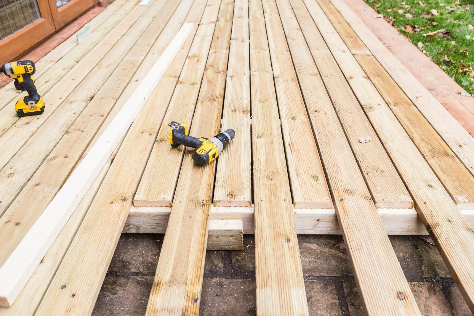 Construction of a wooden deck. Two cordless drills sit on planks. Some planks are laid over supports.