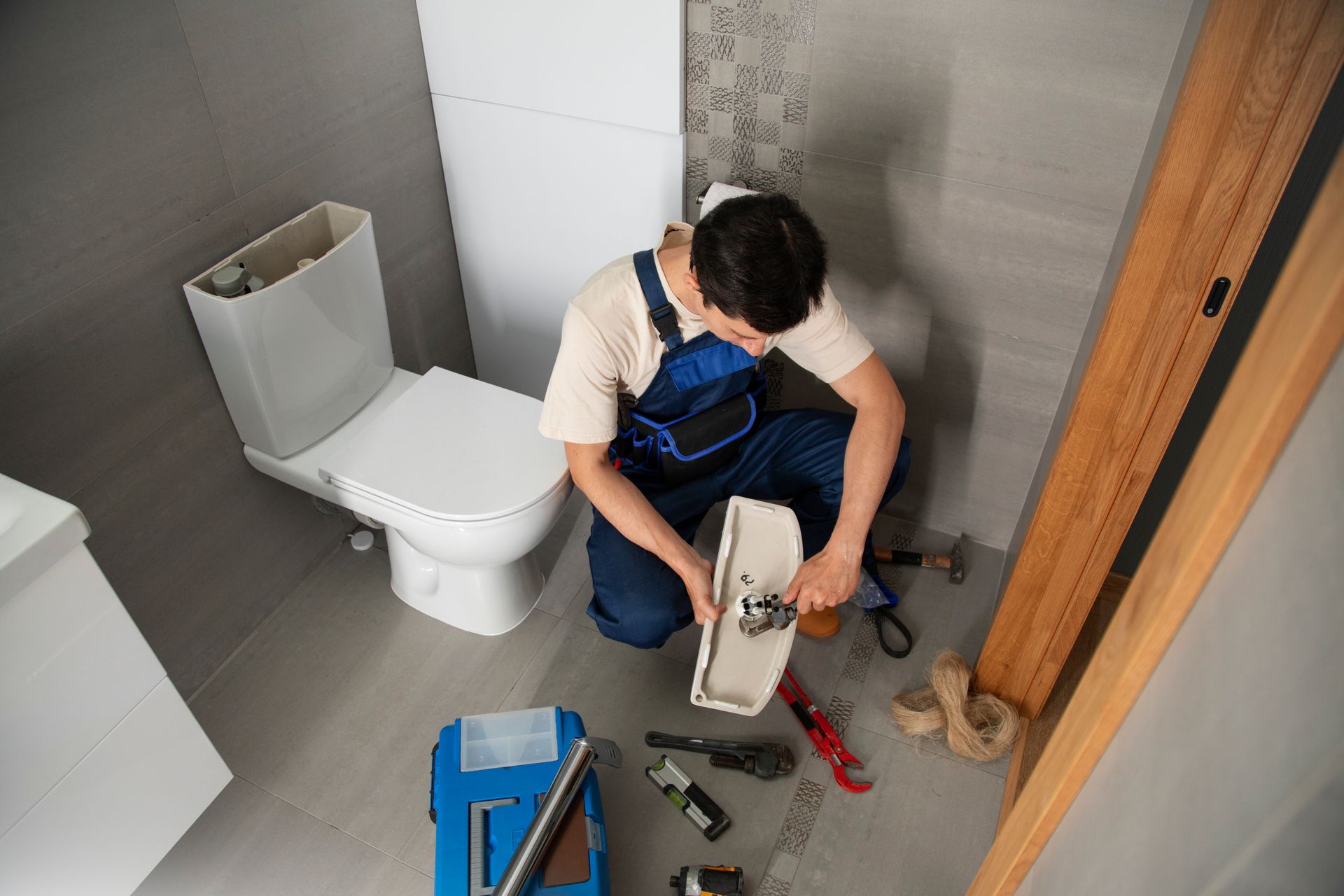 Plumber kneeling, fixing a toilet in a bathroom with tools scattered around.