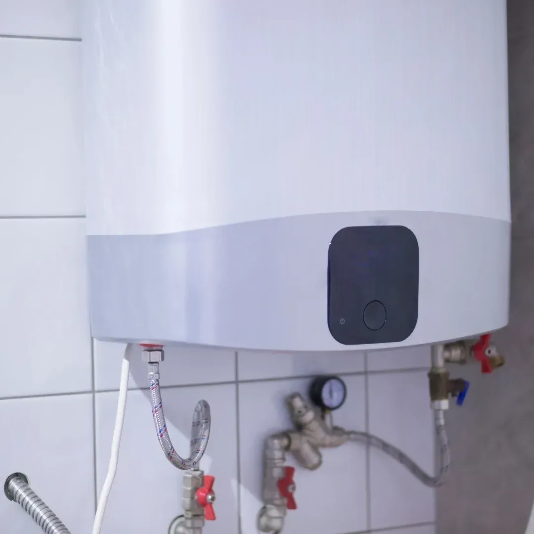 Wall-mounted white water heater with pipes and valves in a tiled utility area