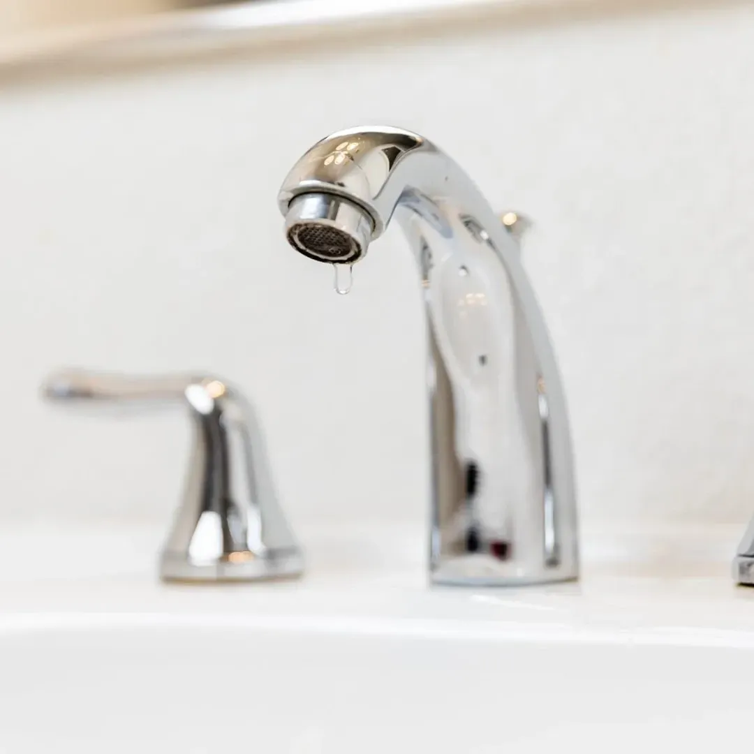 Chrome bathroom faucet and sink spout over a white basin with leaking faucet.