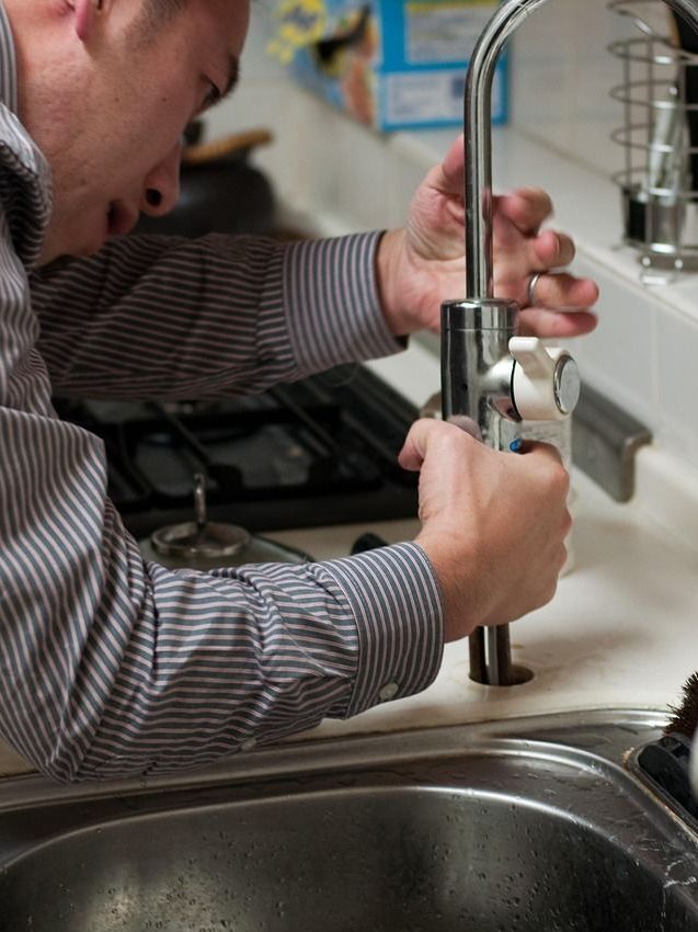 Man fixing a kitchen faucet, wearing striped shirt, close-up.