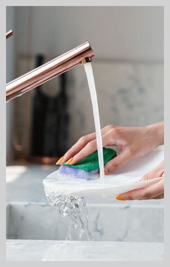 A person is washing a plate in a sink with a sponge.