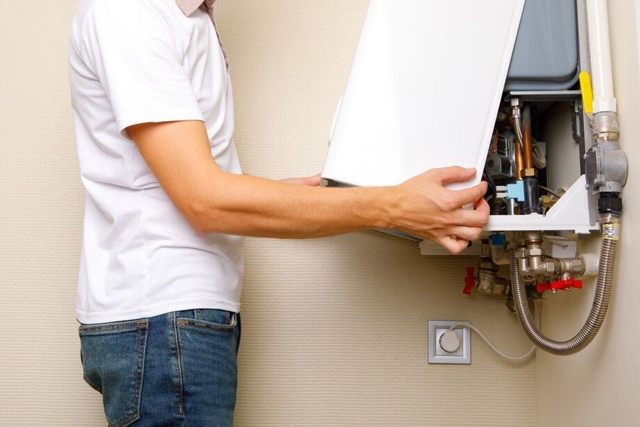 A man is fixing a water heater in a bathroom.