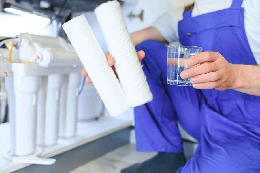 A man in a blue apron is holding a glass of water and a filter.