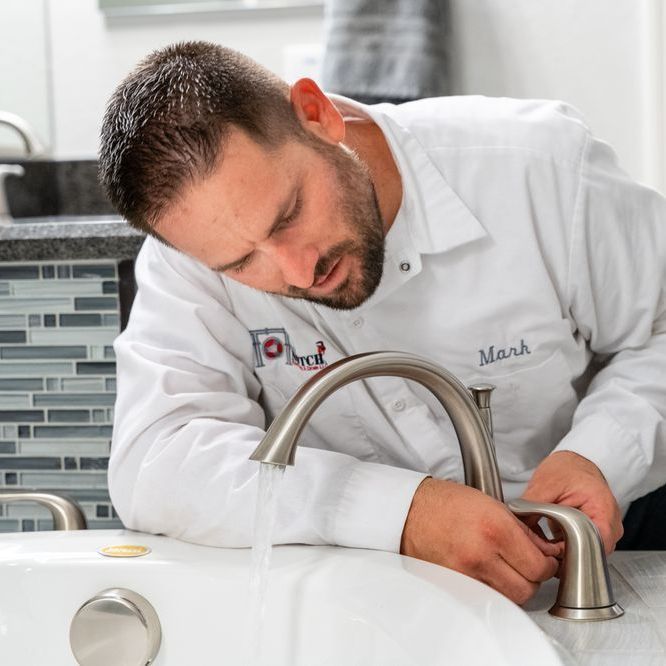A man with the name mark on his shirt is fixing a faucet
