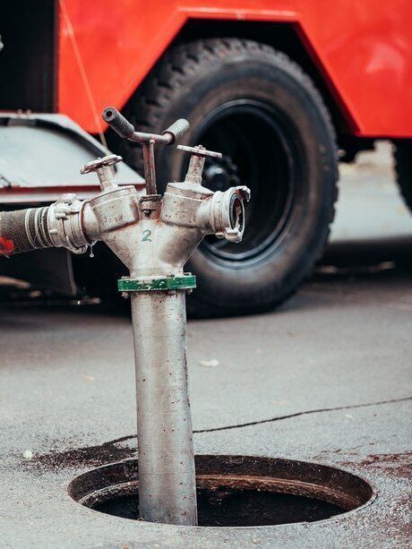 A hose is emerging from a sewer line next to a red truck.