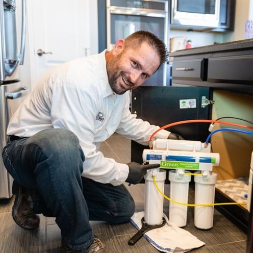 A man is working on a water filter in a kitchen.