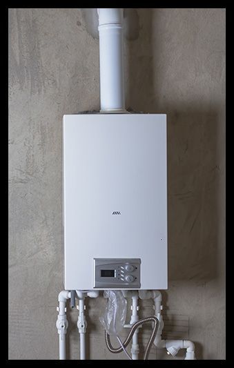 A white boiler is hanging on a wall next to pipes.