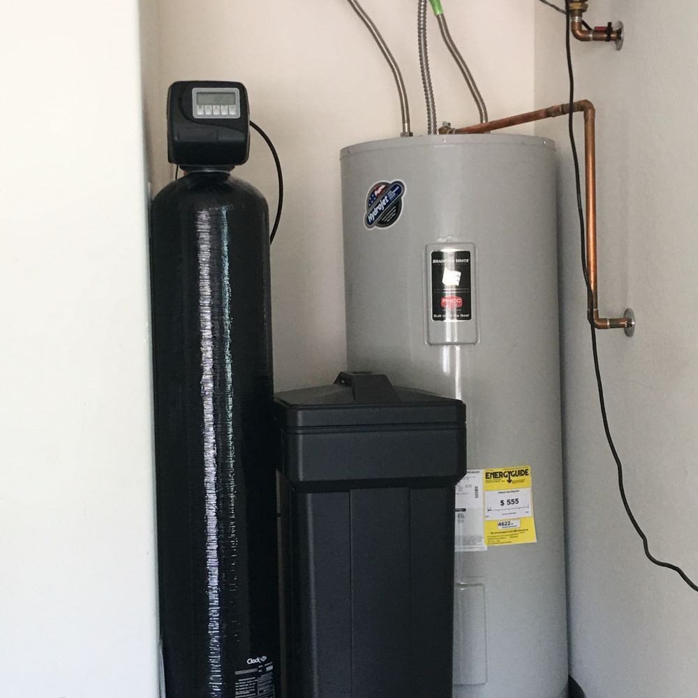 A water heater is sitting next to a water softener in a room.