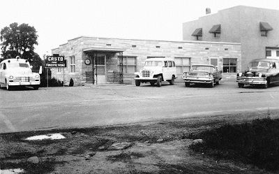 Black-and-white photo of a small roadside building with parked cars and trucks in front