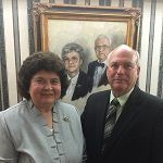 Two people posing indoors in front of a framed portrait.