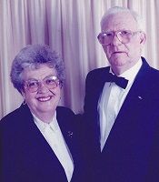 Two formally dressed people smiling against a purple backdrop