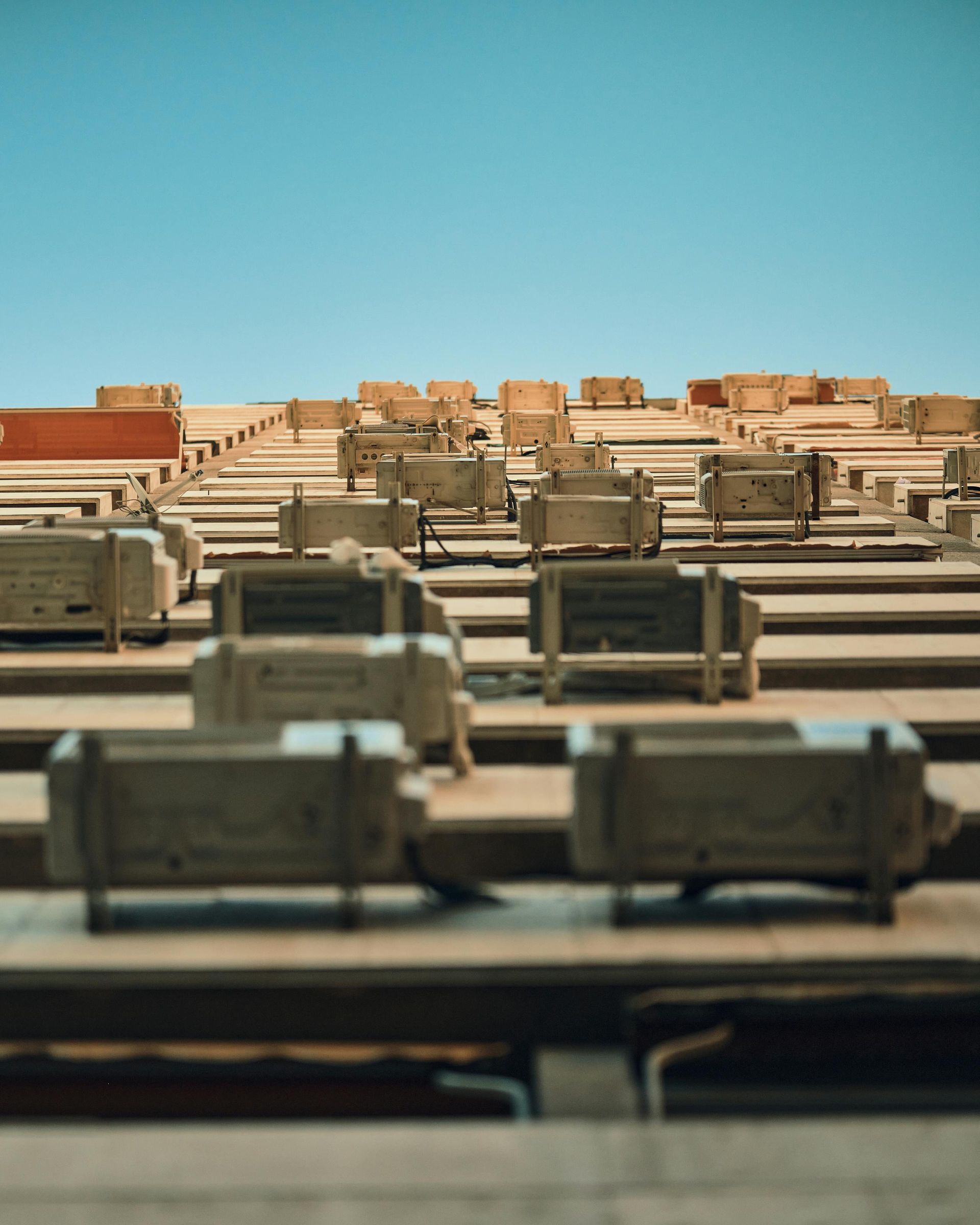 A low-angle view of rows of multiple air conditioning units mounted on the exterior of a building under a clear blue sky.