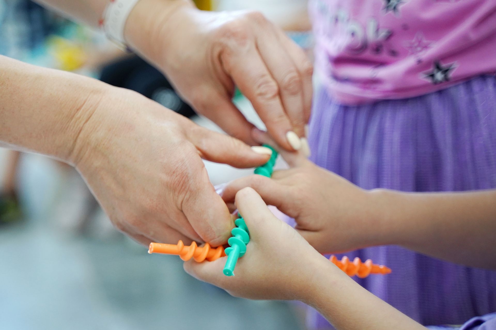 Adult assisting a child’s hands with colorful sensory toy pieces during a therapy activity. Adult assisting a child’s hands with colorful sensory toy pieces during a therapy activity.