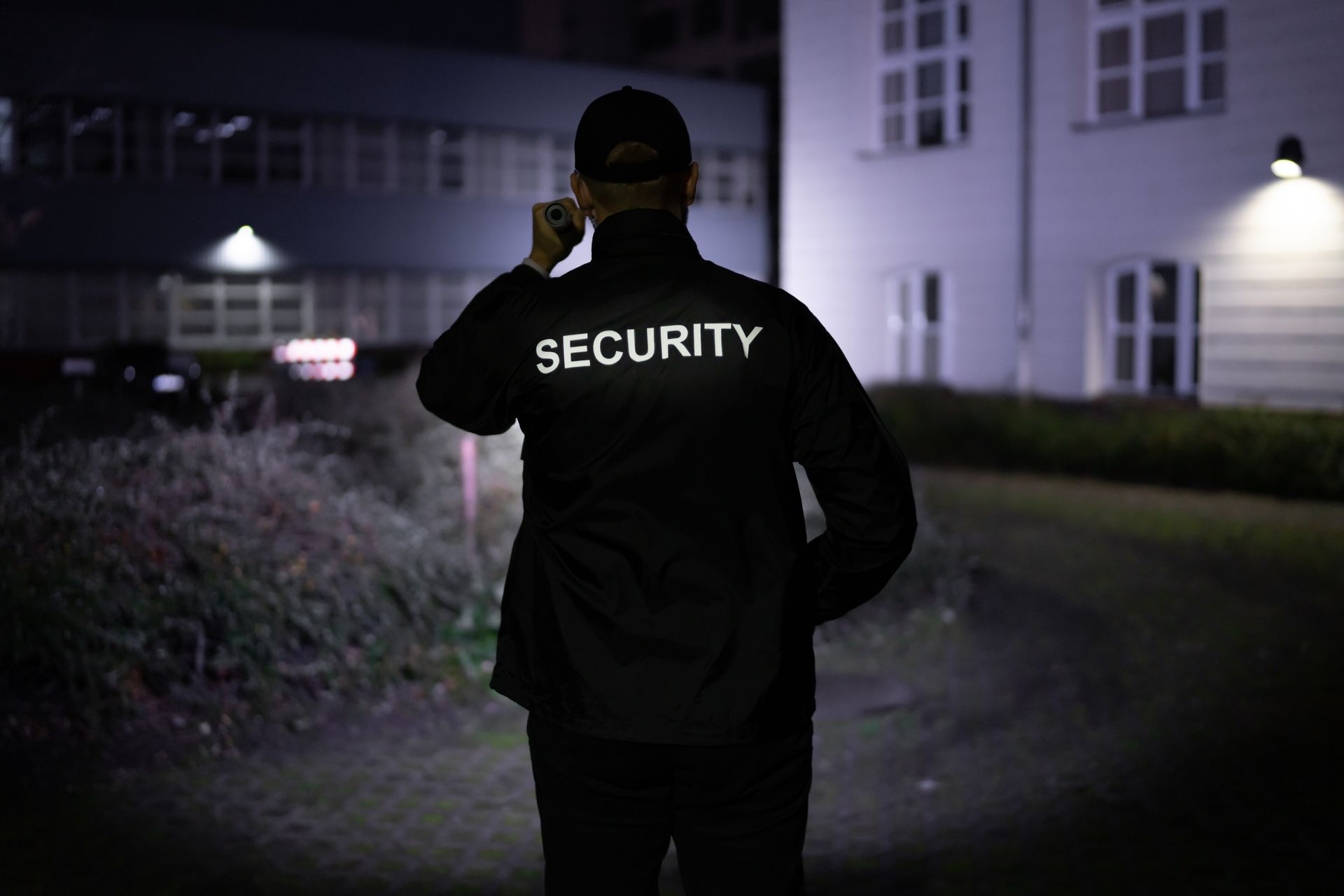 Security Guard Walking Building Perimeter With Flashlight At Night.