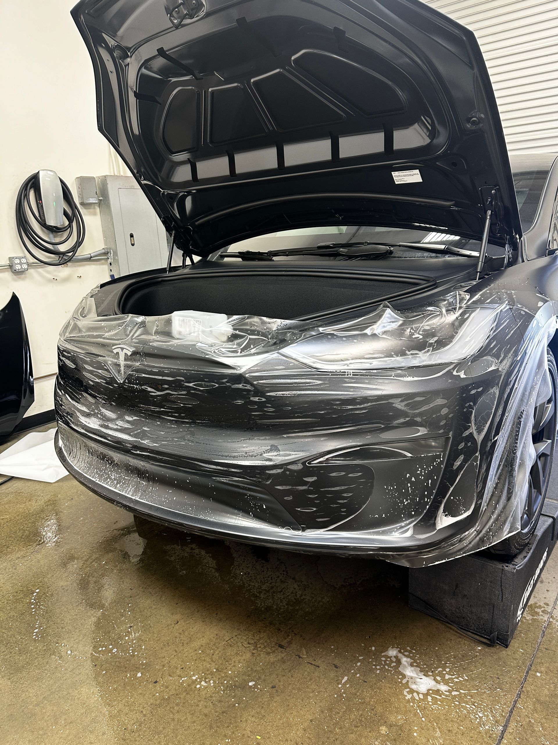 A black car with the hood open is wrapped in plastic.
