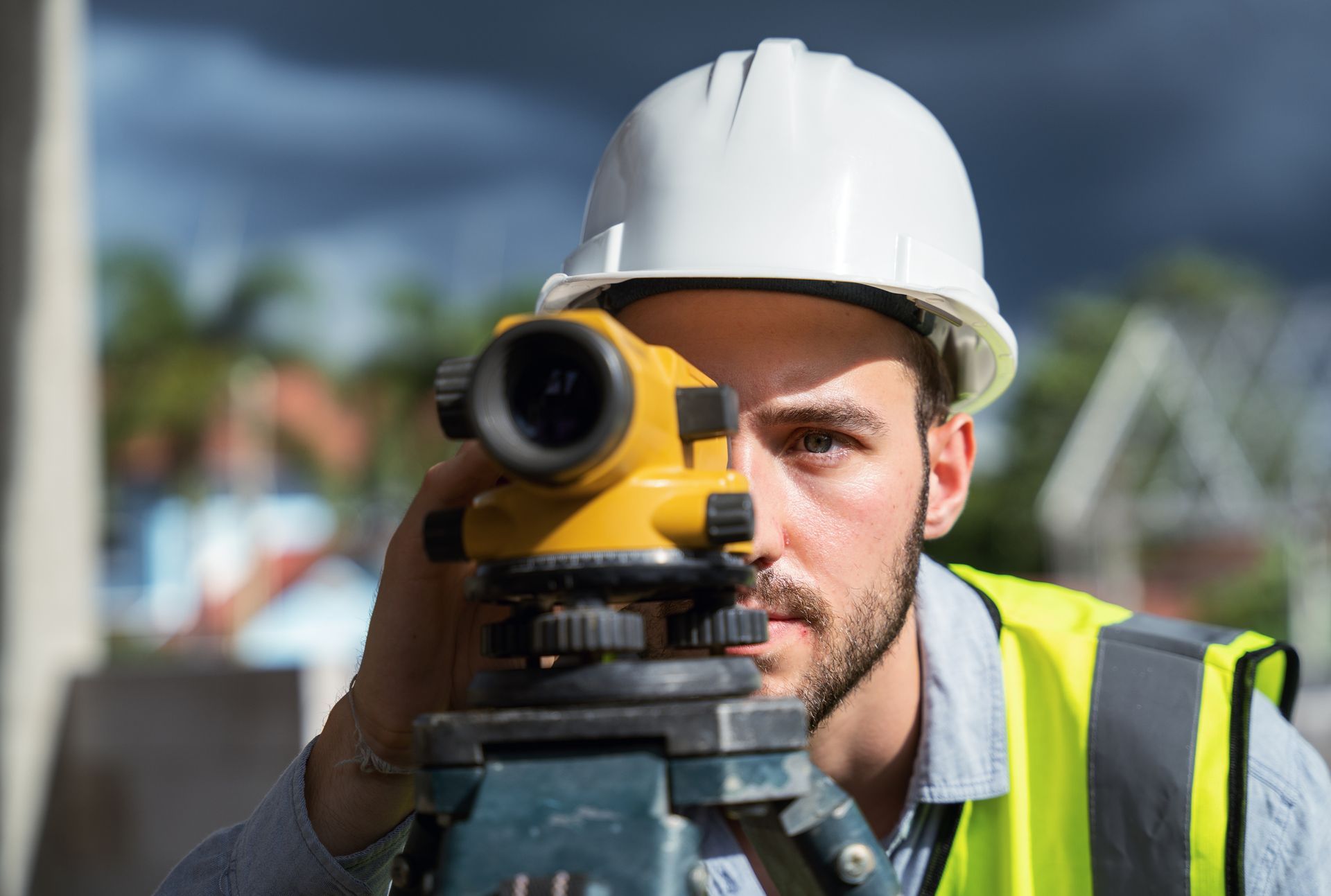 A man wearing a hard hat and safety vest is looking through a level.