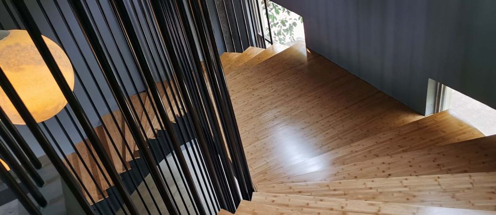 Pianerottolo interno moderno con pavimento in legno curvato, listelli verticali scure e un grande lampadario rotondo.