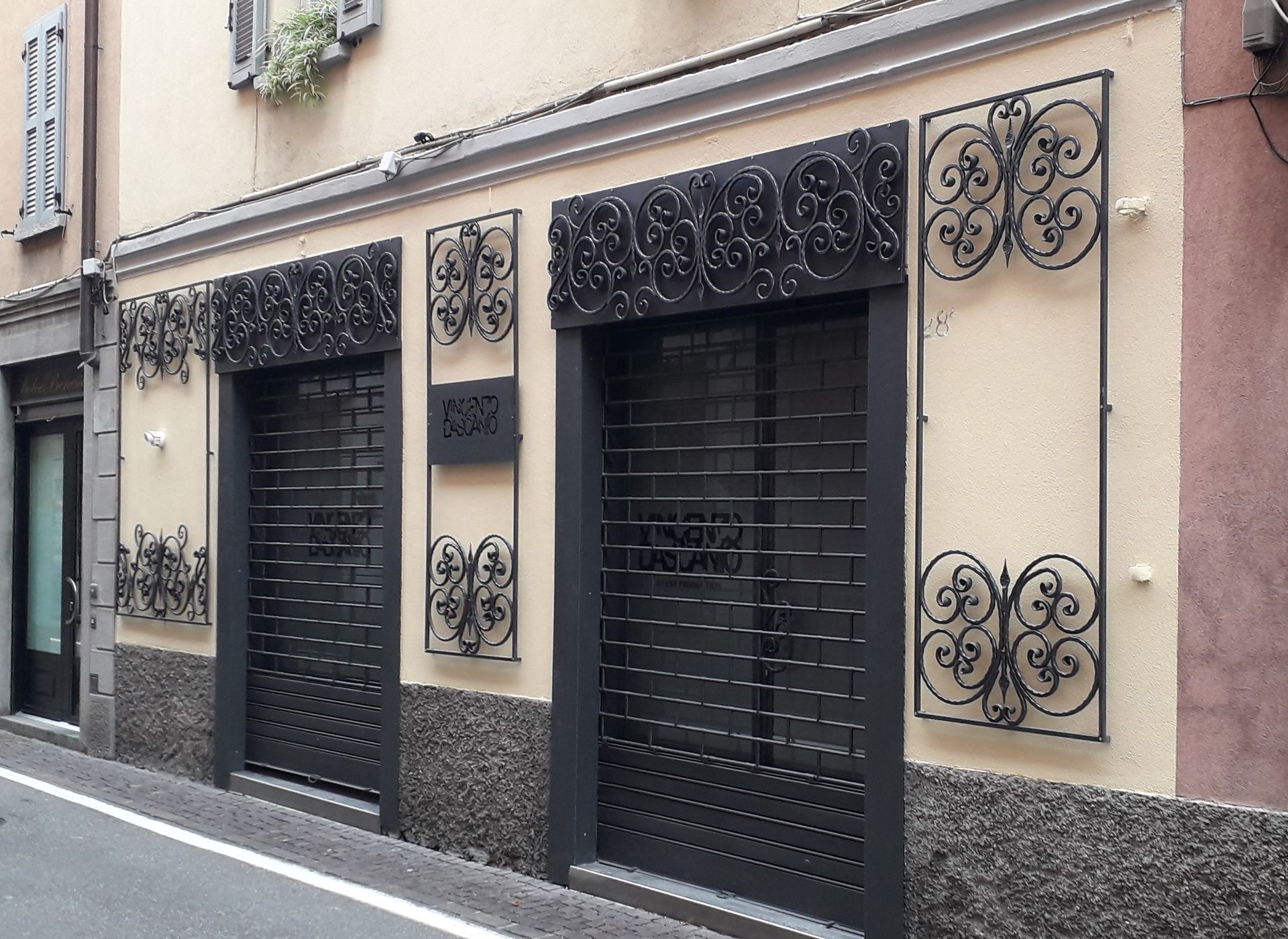 Vista a livello stradale della facciata di un edificio beige con finestre con persiane nere e balconi decorativi in ​​ferro battuto.