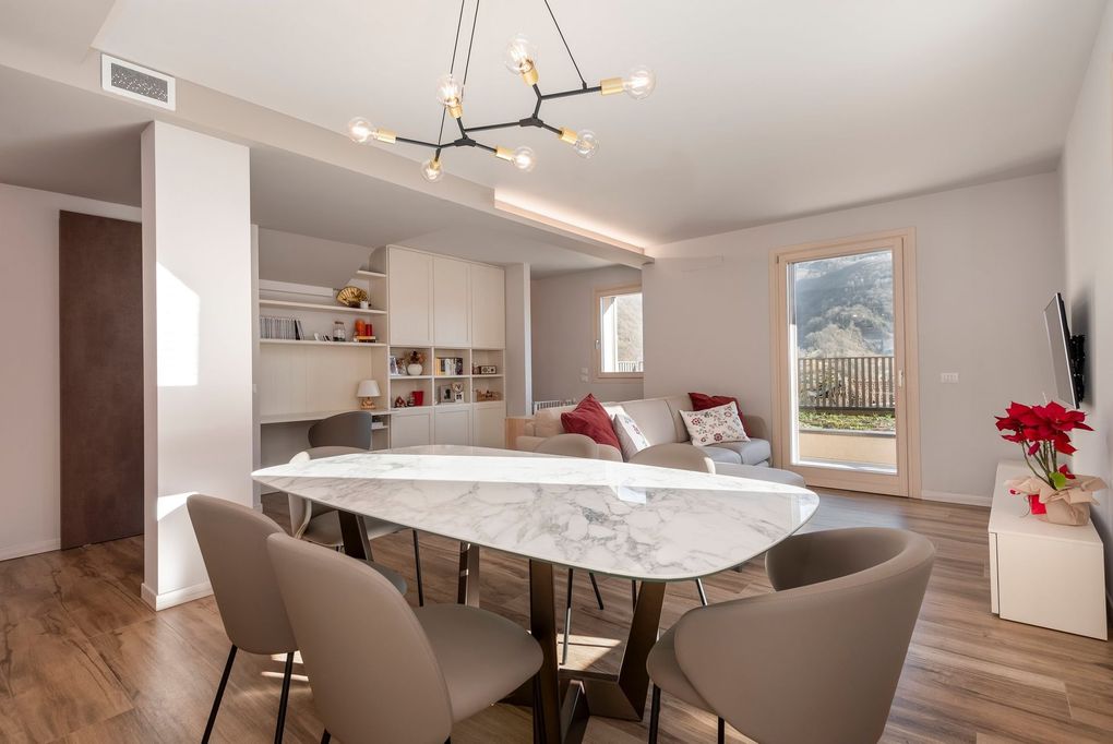 Sala da pranzo moderna con tavolo in marmo, sedie beige, mensole bianche e porta scorrevole in vetro che dà su un balcone.
