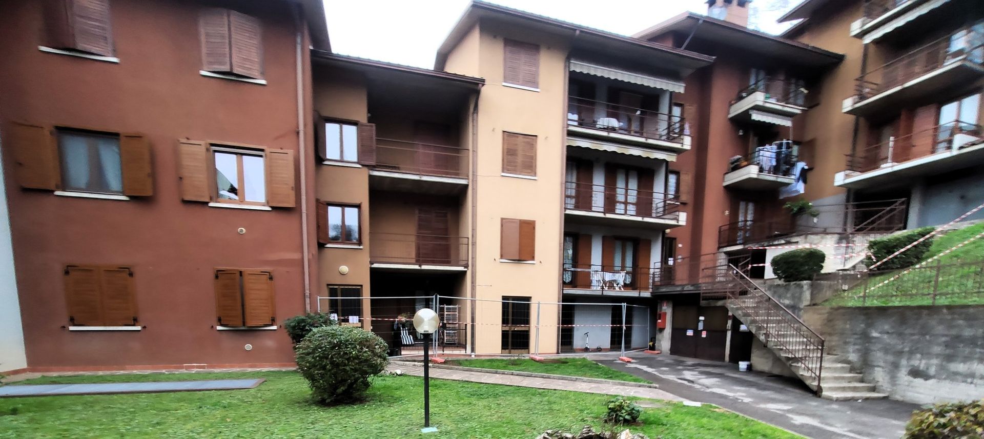 Edifici residenziali con balconi che si affacciano su un piccolo cortile verde e un vialetto pavimentato.