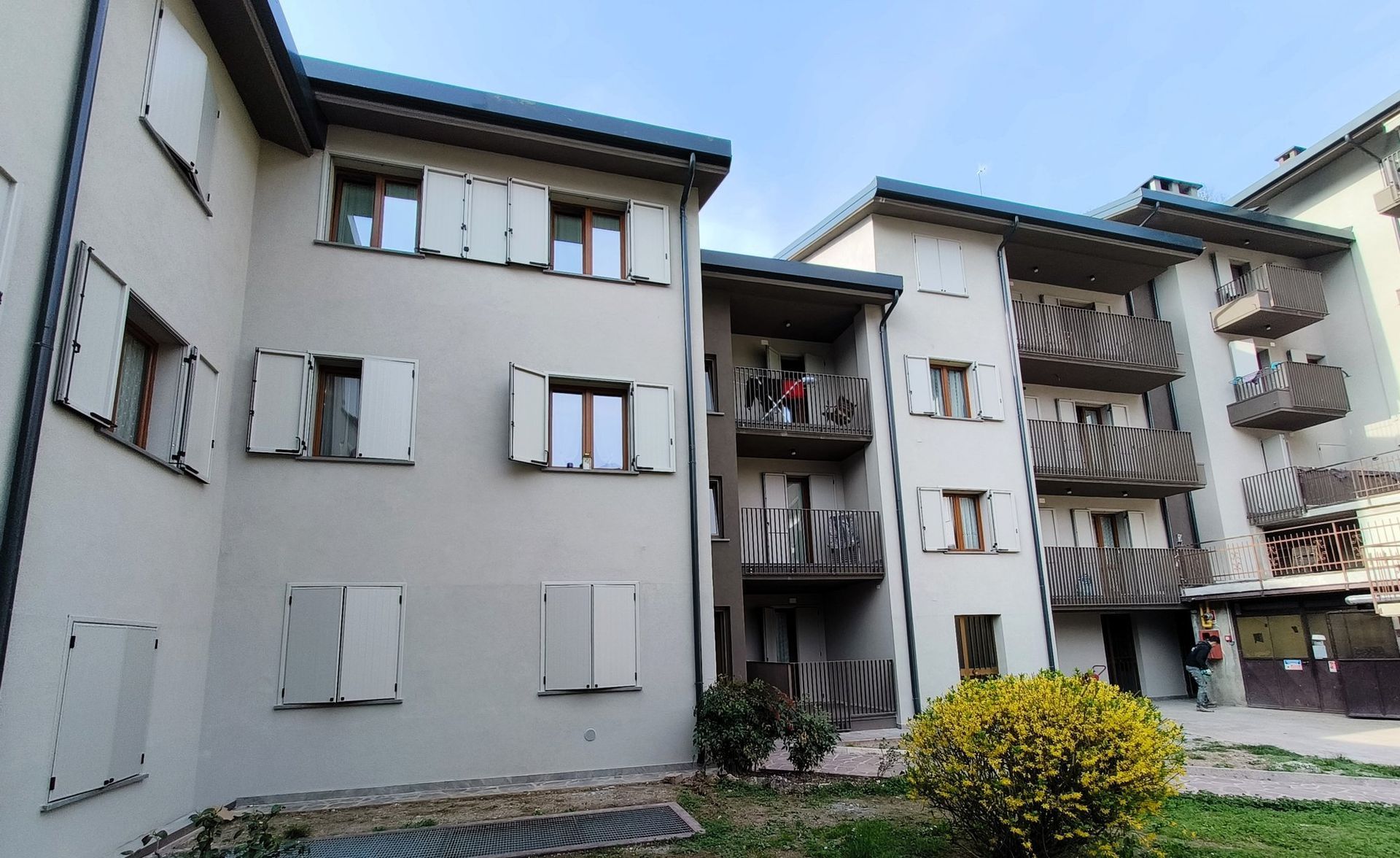 Cortile di un condominio con facciate bianche, balconi e persiane chiuse che circondano un piccolo giardino.