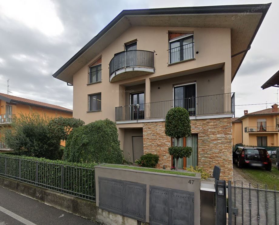 Casa beige a due piani con balcone, cancello d'ingresso e vegetazione ben curata, situata in una strada residenziale.
