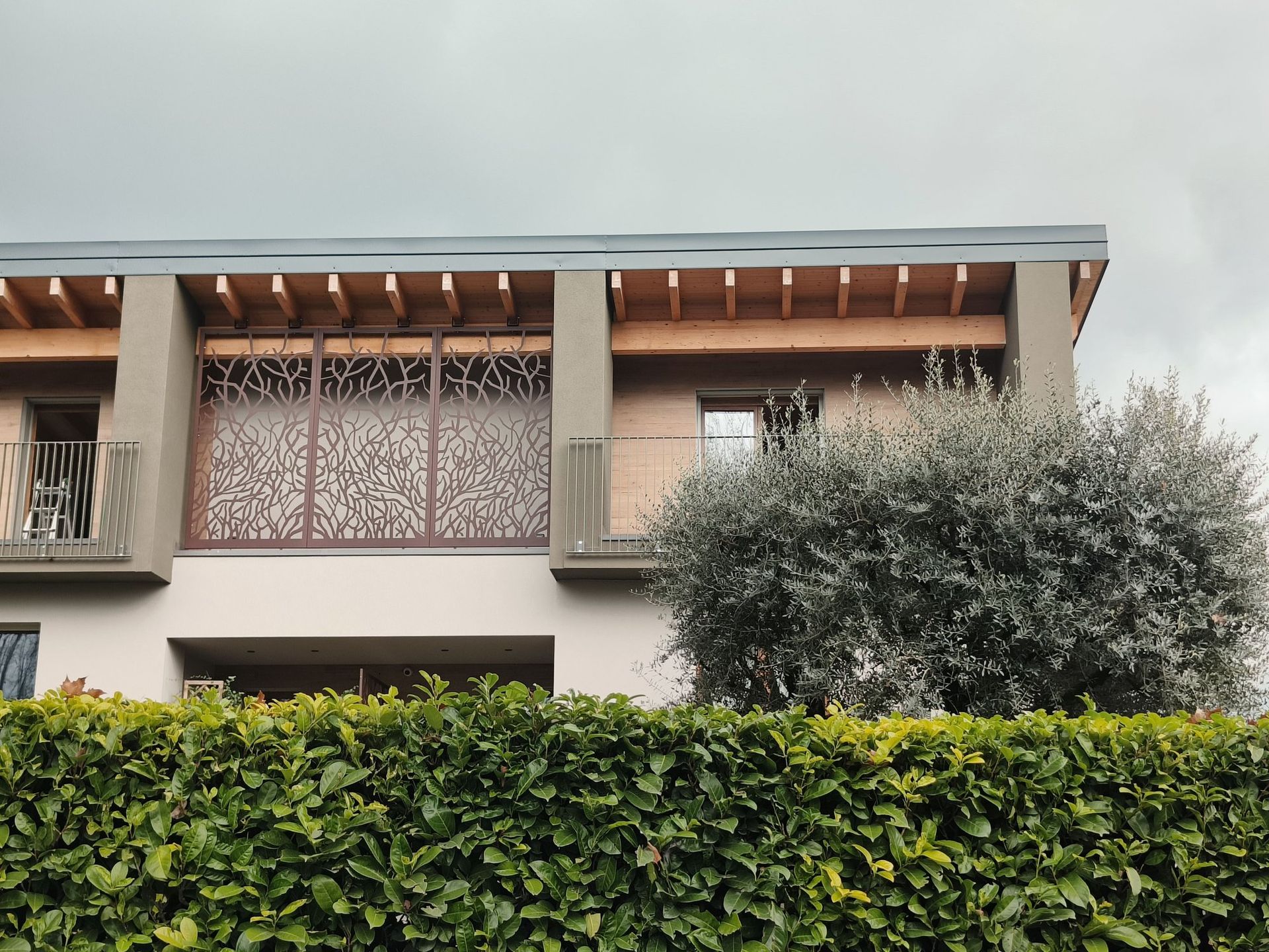 Facciata di una casa moderna con paraventi decorati sul balcone, una siepe e un grande cespuglio sul davanti.