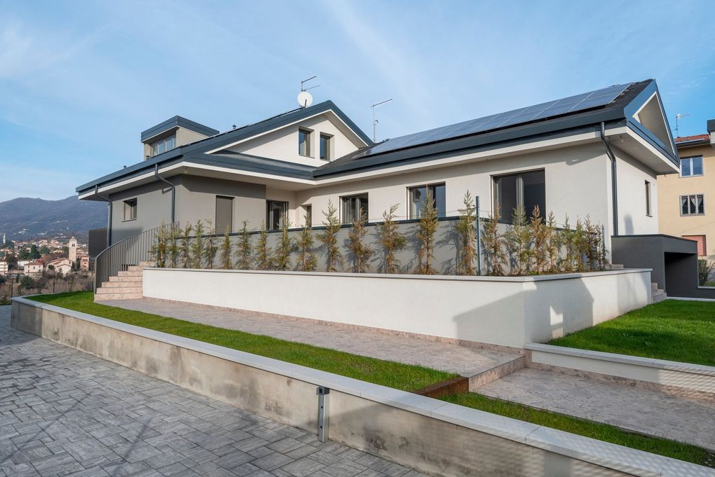 Casa moderna con tetto spiovente e parete bianca, affacciata su una strada lastricata, con le montagne sullo sfondo.